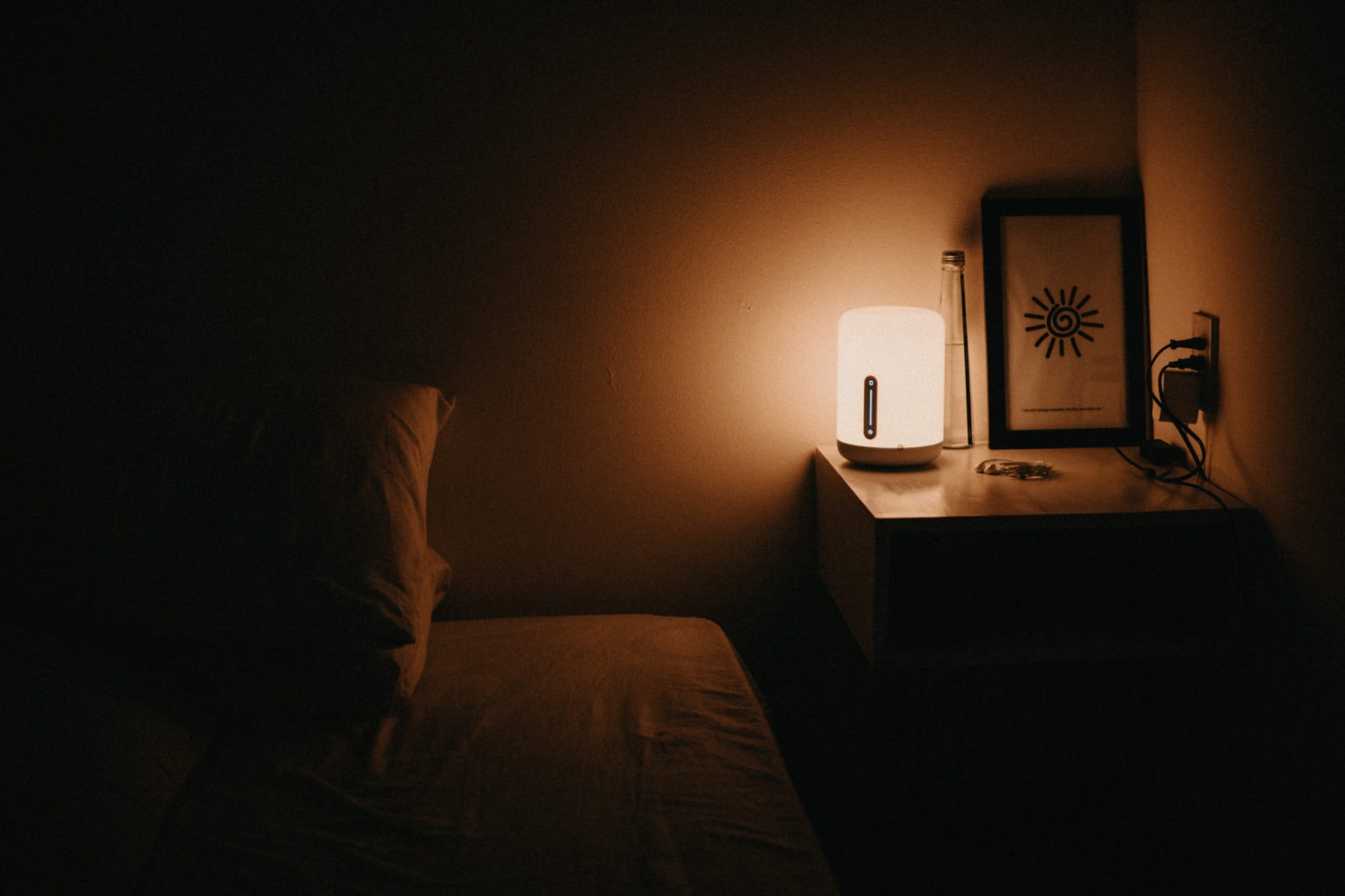 Habitación oscura con una cama, mesa de noche y lampara